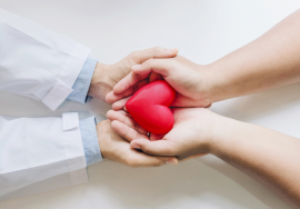Zwei Menschen halten gemeinsam ein rotes Herzsymbol in ihren Händen – Symbol für Vertrauen, medizinische Fürsorge und das Arzt-Patienten-Verhältnis.